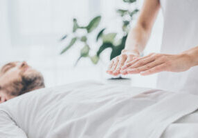 cropped shot of bearded man lying and receiving reiki treatment on stomach